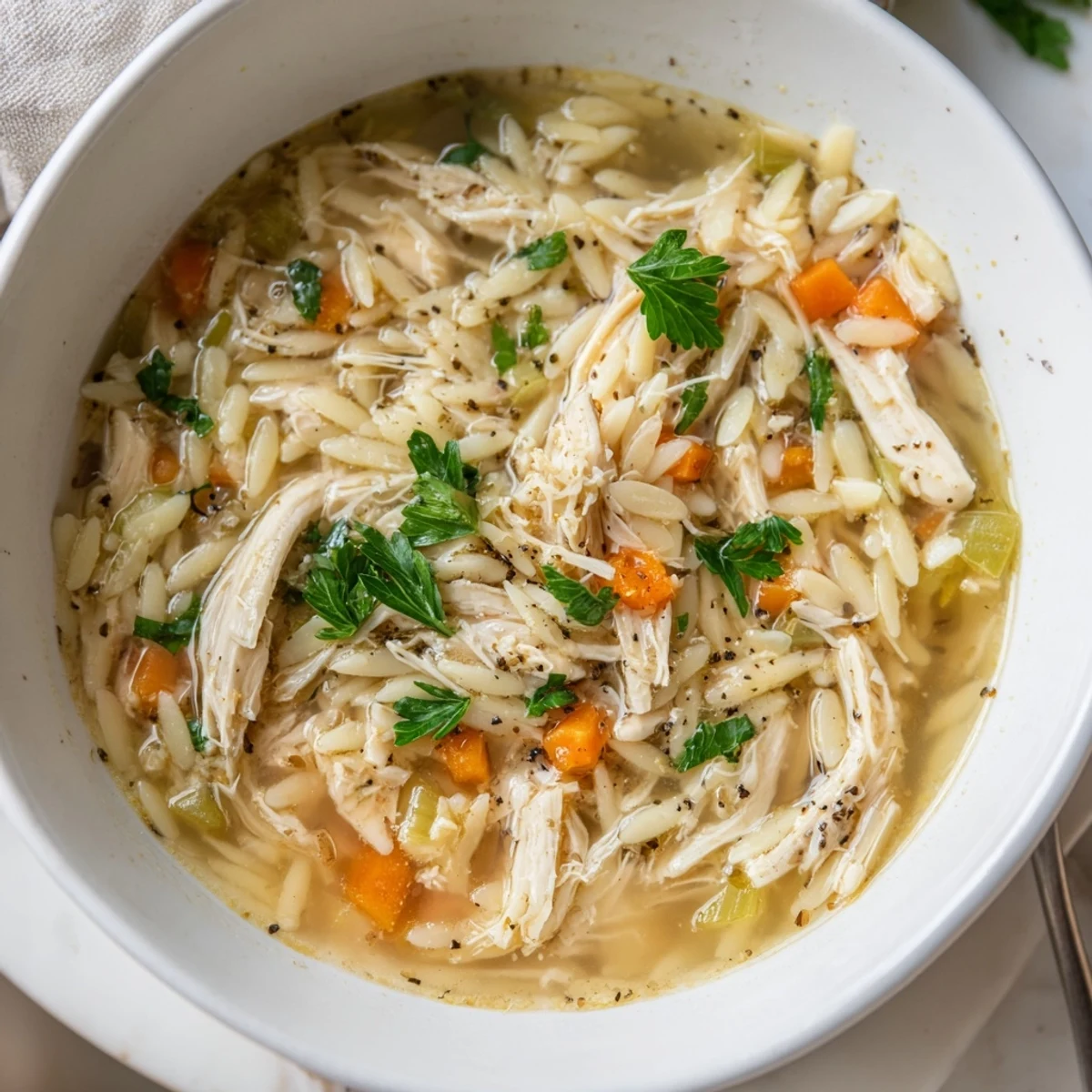 A steaming bowl of Lemon Pepper Chicken Orzo Soup with tender shredded chicken, orzo pasta, and fresh parsley garnish.
