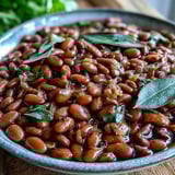 Creamy pinto beans simmered with aromatics and bay leaves, served warm as a hearty vegan side dish.