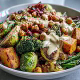 A vibrant bowl of Roasted Veggie & Chickpea Bowls featuring roasted sweet potatoes and Brussels sprouts drizzled with sweet, tangy tahini sauce.