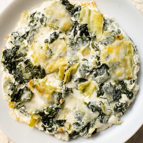 A close-up of Spinach Artichoke Dip, beautifully browned and served with crisp tortilla chips.