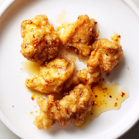 A close-up view showcases the glistening hot honey butter sauce clinging to the crunchy, perfectly fried chicken pieces.  