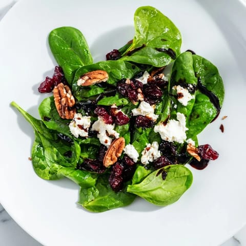 A vibrant spinach goat cheese salad tossed in a tangy balsamic vinaigrette, served on a white plate for a light lunch or elegant starter.  