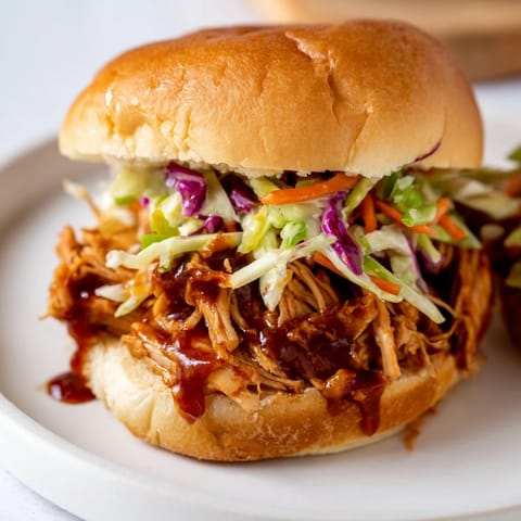 Savory BBQ chicken sliders served with tangy slaw and pickles on a rustic wooden board for game day.  