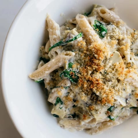 Fresh spinach and marinated artichoke hearts nestled in a creamy Artichoke Pasta Bake, ready to serve.