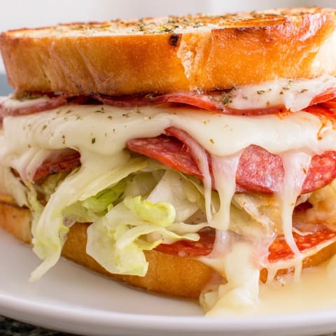 Hearty Italian sub grilled cheese with crispy bread, melted provolone, and a colorful lettuce topping, served beside kettle chips.  