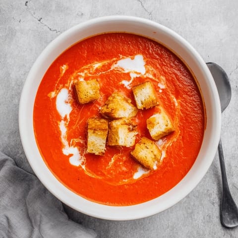 Hot Roasted Tomato Soup With Crispy Croutons is garnished with fresh thyme and served alongside crusty artisan bread for a comforting lunch.