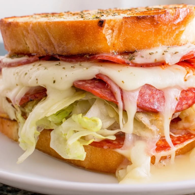Hearty Italian sub grilled cheese with crispy bread, melted provolone, and a colorful lettuce topping, served beside kettle chips.  