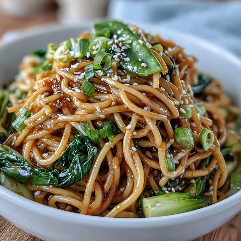 Flavorful Asian-inspired noodle dish featuring ginger-garlic sauce, sautéed greens, and toasted sesame garnish in a steaming bowl.