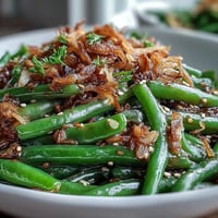 Aromatic green beans sautéed with garlic and sesame, topped with crispy fried onions for a savory side dish.  